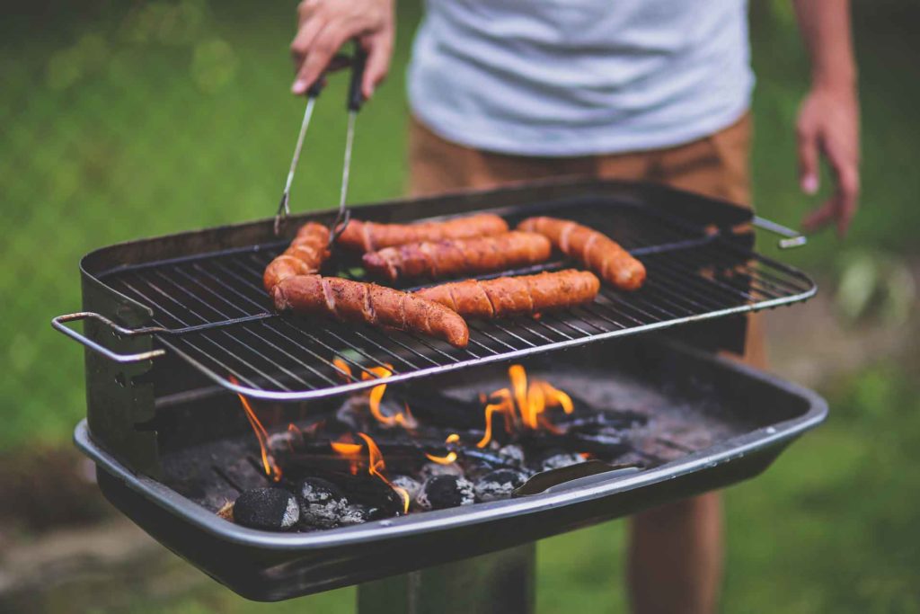 spiralized hotdogs on a charcoal grill with man out of focus