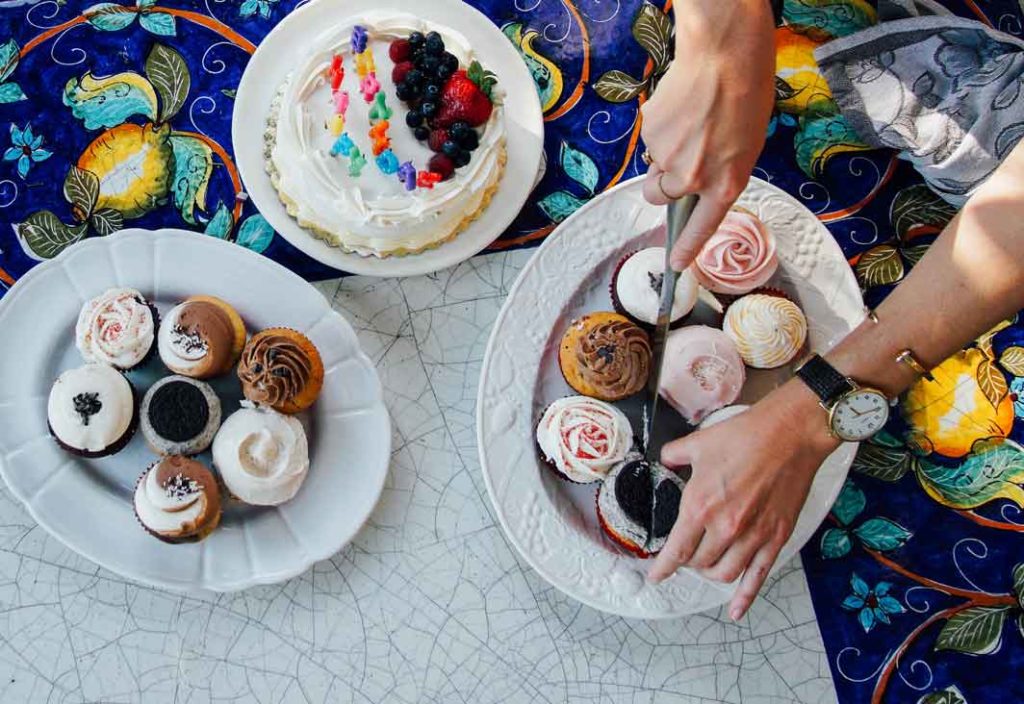 aerial view of woman's hands cutting into various cupcakes