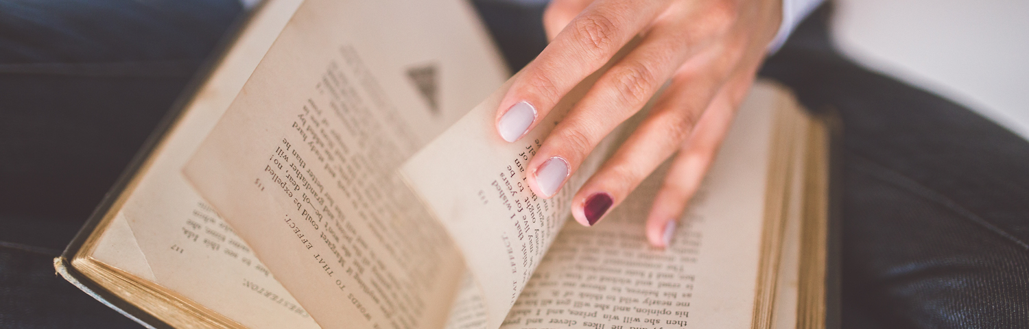 closeup of hand with painted fingernails shuffling through book pages