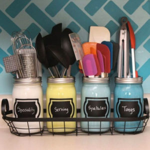 four colorful mason jars holding kitchen utensils on countertop
