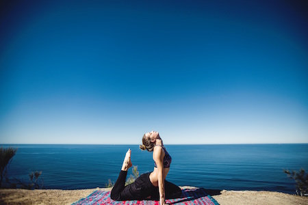 girl doing yoga on a mat with the ocean view behind her