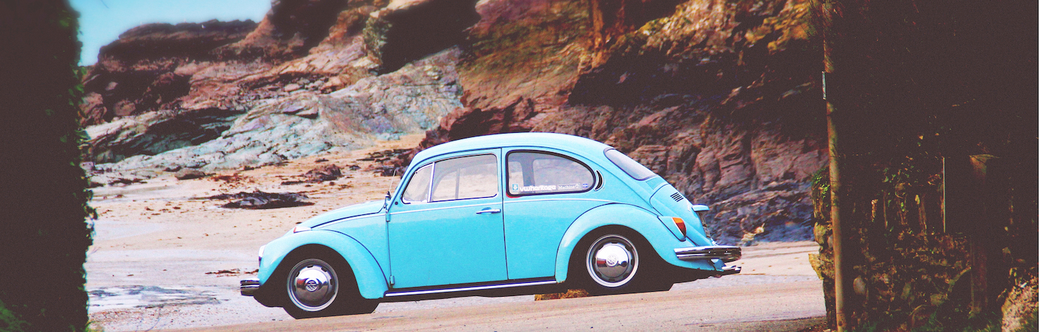 old fashioned blue bug car parked on beach by rocks