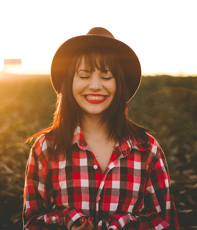 young hipster woman in a field smiling with eyes closed at sunset