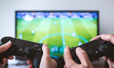 closeup of television displaying sports video game and hands playing with controllers