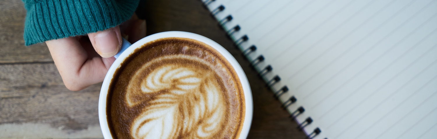 woman's hand holding coffee cup next to an open notebook