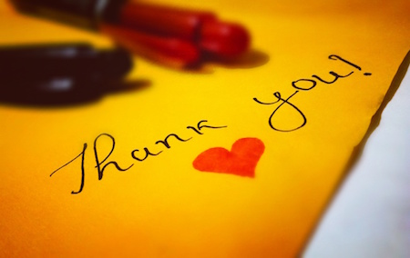 handwritten thank you note on golden orange paper with a heart and red pen in background