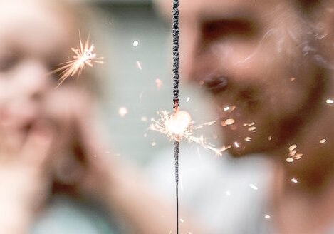 closeup of sparkler with dad holding toddler out of focus in the background