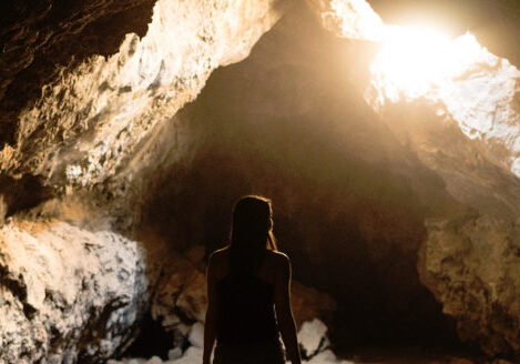 silhouette of a woman standing in cave looking inward sun coming through hole