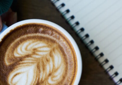 woman's hand holding coffee cup next to an open notebook