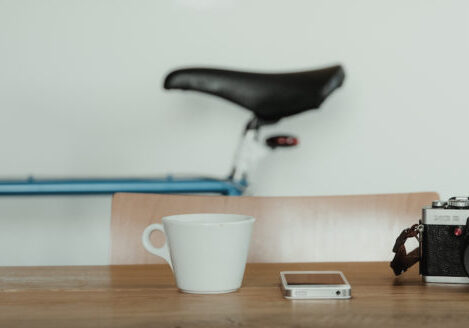 film camera, phone, and coffee on top of a table with a bike against the wall behind it