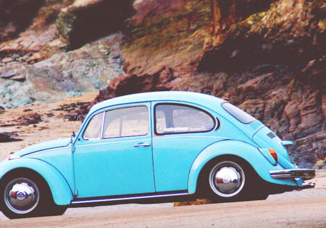 old fashioned blue bug car parked on beach by rocks